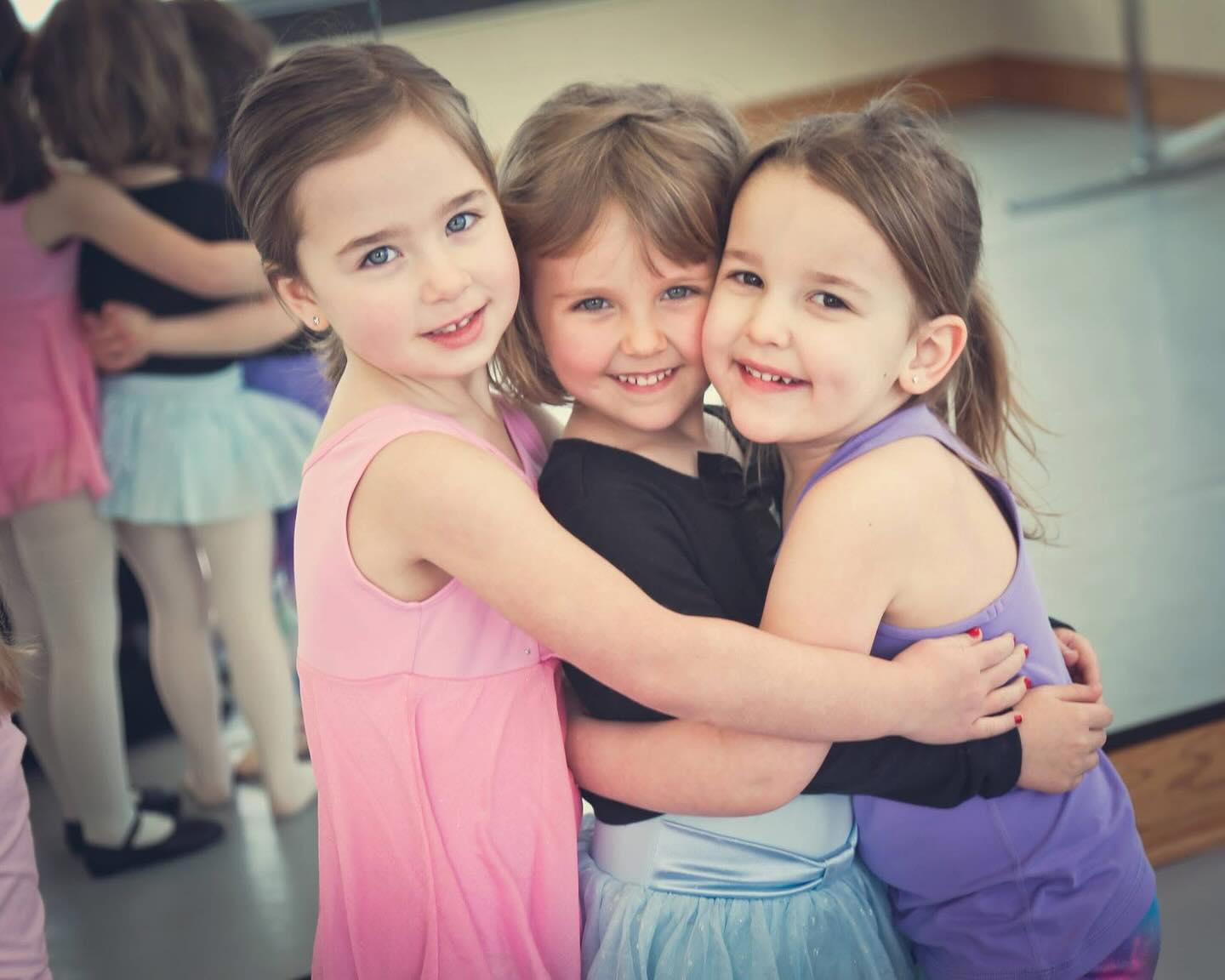 Three young dancers hugging and smiling at The Dance Company studio